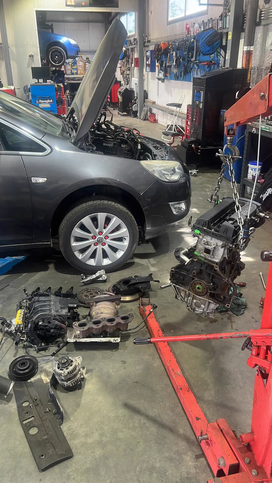 Opel cu motorul scos pe macara, piesele demontate așezate lângă mașină